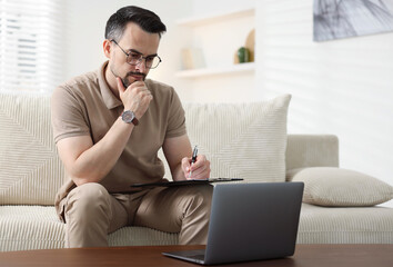 Professional psychologist having online consultation with his client via laptop on sofa indoors....