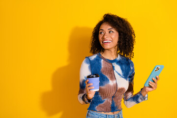 Young woman with a smartphone and coffee cup posing against a vibrant yellow background showcasing...