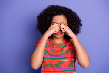 Young woman in colorful striped t-shirt covering her face with hands against a violet background