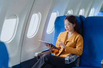 Asian businesswoman traveling by plane using tablet to work and read book to check business report...
