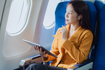 Asian businesswoman traveling by plane using tablet to work and read book to check business report...