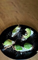 Gourmet avocado and cream cheese toast served on a black plate over wooden table, perfect for healthy breakfast themes.