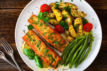 Seared salmon steaks with green string beans and roasted potatoes on wooden table