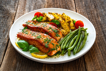 Seared salmon steaks with green string beans and roasted potatoes on wooden table