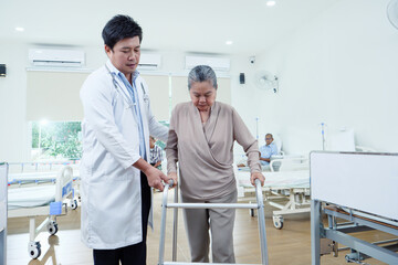 Elderly Asian woman receiving physical rehabilitation from doctor in modern hospital setting, showcasing professional elderly care and support in recovery.