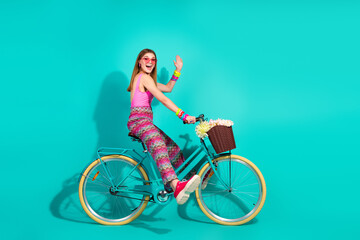 Young woman in stylish retro outfit cycling on a vibrant background with a flower-filled basket,...