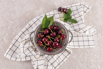 Juicy cherries in colander on checkered cloth from top view
