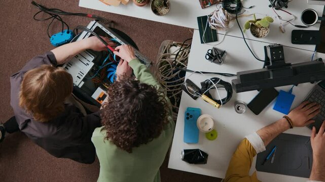 Directly above shot of curly-haired girl helping young man to install cooling fan in PC case, unknown male programmer working on computer at cluttered desk