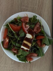 Fresh salad with sliced tomatoes, mozzarella, and leafy greens on a plate over wooden table, perfect for healthy food visuals.