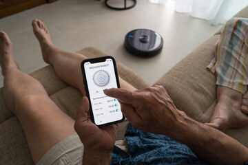 Senior man operating smart vacuum using smartphone app