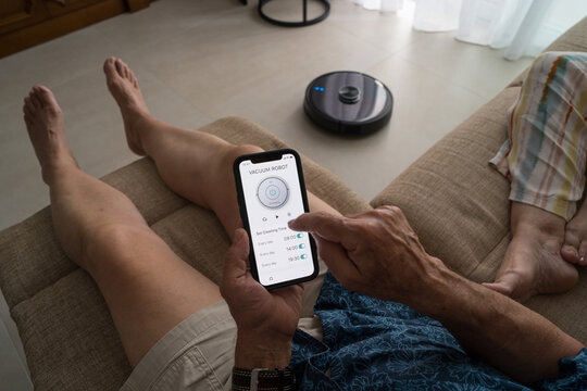 Senior man operating smart vacuum using smartphone app
