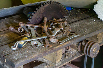 collection of old rusty hand tools, wrenches, and a circular saw blade scattered on a worn wooden workbench in a vintage workshop. Aged and abandoned atmosphere with visible signs of corrosion and dec