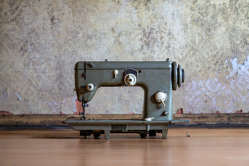 Old industrial sewing machine standing on the floor of an abandoned house, placed against a...