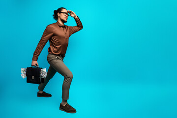 Young businessman with briefcase of money posing stylishly against a vibrant background, expressing...