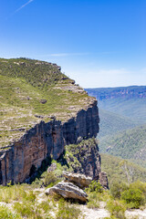 Walls Lookout, a panoramic view of the Blue Mountains National Park in New South Wales, Australia, featuring a lush valley, rugged cliffs, and a clear blue sky.