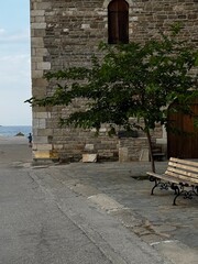 A traditional Greek stone structure with benches and tree, overlooking the sea, ideal for heritage, travel, and architectural content.