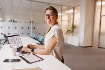 A young woman focuses on her laptop in a bright, modern office that inspires her creativity and...