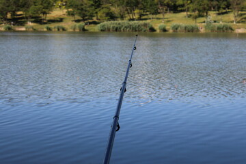 Fishing rod over a calm lake with trees.