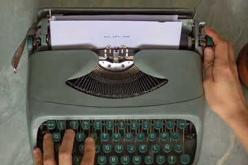 Hands typing on a vintage typewriter with the phrase live, love, laugh written on the paper,...