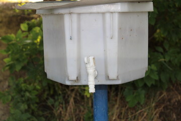 White plastic water tank with tap outdoors.