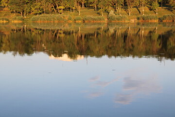 Calm lake reflecting trees and sky at sunset.