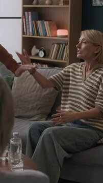 Vertical of middle-aged Caucasian couple arguing during couples therapy session in front of unrecognizable psychologist with husband going away avoiding conversation