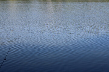 A tranquil lake with a fishing rod and bobber visible on the water.