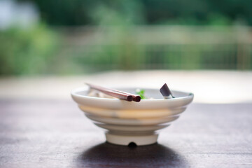 Close-up of a white ceramic bowl with tea utensils including a spoon and a tea scoop on a wooden...