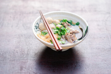 Traditional Asian Chicken Noodle Soup in a White Ceramic Bowl with Vegetables and Chopsticks on Rustic Wooden Surface