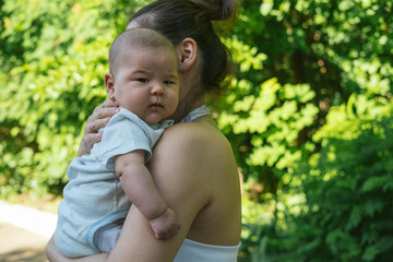 Young Asian mother is holding cute boy son and kissing his cheeks with love and tenderness. Newborn...
