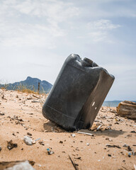 Plastic jerry can washed ashore on a deserted sandy beach with mountain in the distance, symbolizing marine pollution and environmental degradation. Concept of ocean waste and coastal contamination.