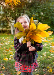 Little girl holding yellow autumn leaves, smiling outdoor park. Seasonal joy child happiness concept