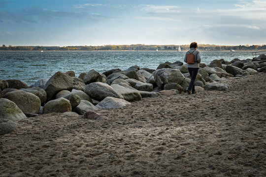Eine Frau macht im Sp&auml;therbst am Brodtener Ufer in der L&uuml;becker Bucht einen Strandspaziergang; im Hintergrund der langgezogene Sandstrand des Priwalls; in der Ostsee Segler auf dem Weg zum Hafen