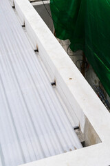 Close up view shows white corrugated sheet secured to metal frame detail from construction site utilizing foam insulation potentially with pu properties suggesting protection from elements