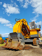Heavy machinery excavator with bright yellow exterior parked on construction site under blue sky