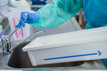 Close-up of a scientist in protective gear, turning on the tap above a stainless steel sink with a...