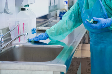 Gloved hand in protective uniform meticulously wiping a stainless steel counter, demonstrating...