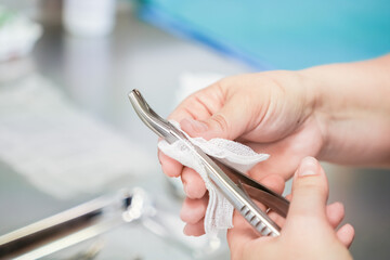 Close-up of healthcare professional hands meticulously wiping a stainless steel surgical tool with...