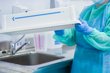 Medical worker in blue gloves and gown holds a white container marked 7.5 L, preparing for...