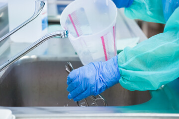 A healthcare professional meticulously cleans medical tools in a sterile stainless steel sink,...