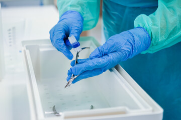 Close-up of gloved hands meticulously cleaning a medical instrument with a brush over a white...