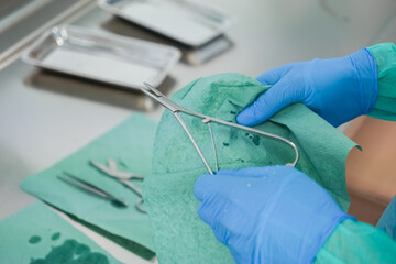 Detailed close-up of hands in blue medical gloves meticulously wiping a surgical instrument with a...