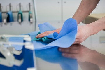 Close-up view of hands carefully arranging blue and teal sterile drapes on a clean metallic...