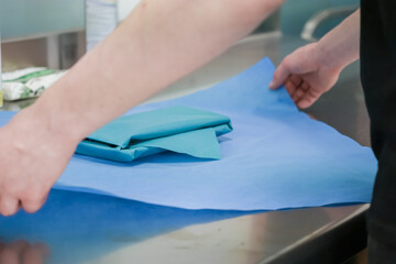 Close-up of a healthcare professional's hands carefully folding sterile blue fabric around...