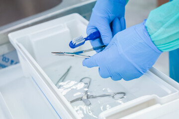 Close-up of gloved hands performing detailed cleaning of metal medical tools in a liquid solution,...