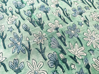 A close-up of light blue cotton fabric showcases tiny, outlined floral block prints in a graceful,...