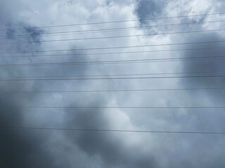 The image captures electrical power lines stretching across a cloudy sky, creating a stark, linear...