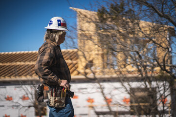 Male Construction Worker Wearing Texas Hard Hat and Tool Belt Looking Out at House Under...