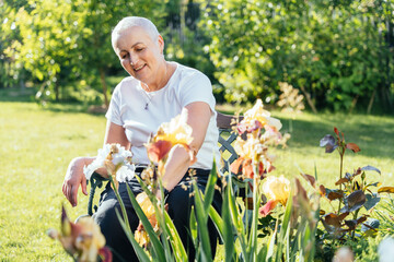 Senior woman sitting on bench and admiring flowers in garden