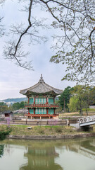 The beautiful Hyangwonjeong Pavilion stands on an island in a tranquil pond at Gyeongbokgung Palace. Spring trees frame the traditional Korean architecture under a cloudy sky. Seoul, South Korea.